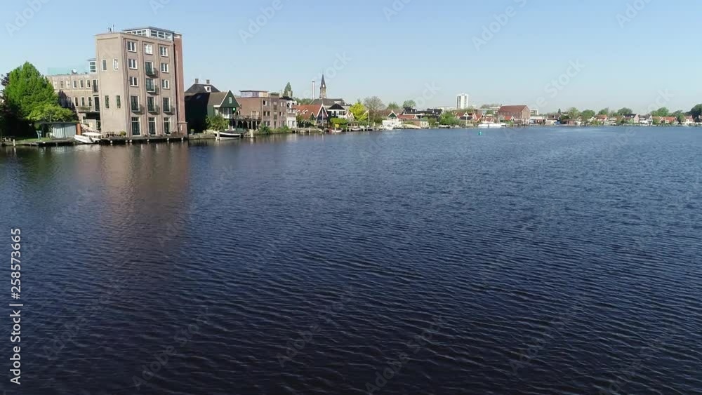Flight between windmills, drone flight just above the water . Aerial view of Zaanse Schans, Zaandam near and Amsterdam Netherlands and typical Dutch town with colorful houses, during sunny day. Flight between windmills, drone flight just above the water . Aerial view of Zaanse Schans, Zaandam near and Amsterdam Netherlands and typical Dutch town with colorful houses, during sunny day.