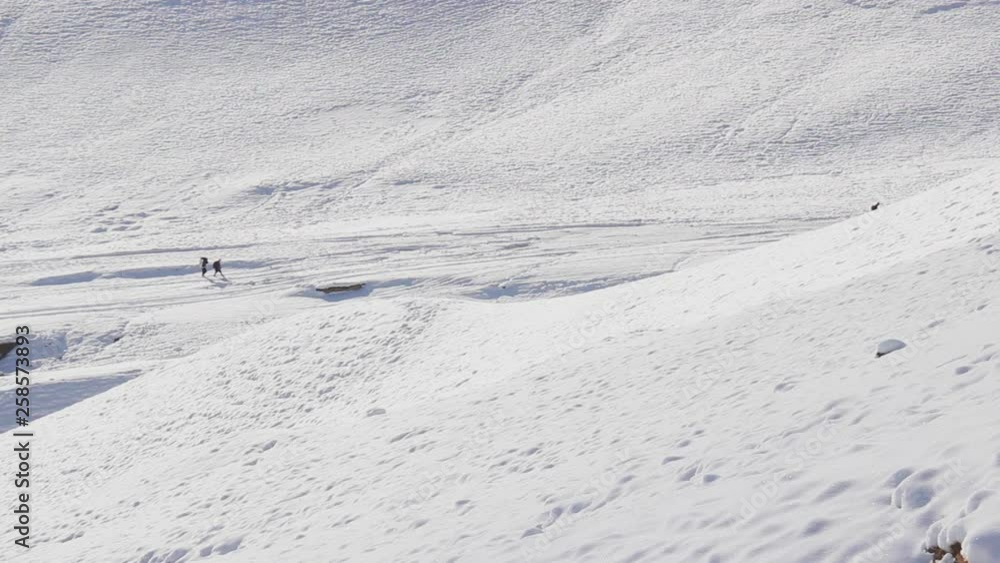 Beautiful shot looking down on 3 people trekking on snow filled mountain landscape in Nepal Mustang Chhosar Beautiful shot looking down on 3 people trekking on snow filled mountain landscape in Nepal Mustang Chhosar
