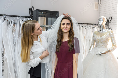 Saleswoman fitting veil for young bride in store