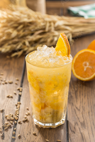 fresh squeeze natural orange juice in clear drinking glass and wheat spikes on wooden table