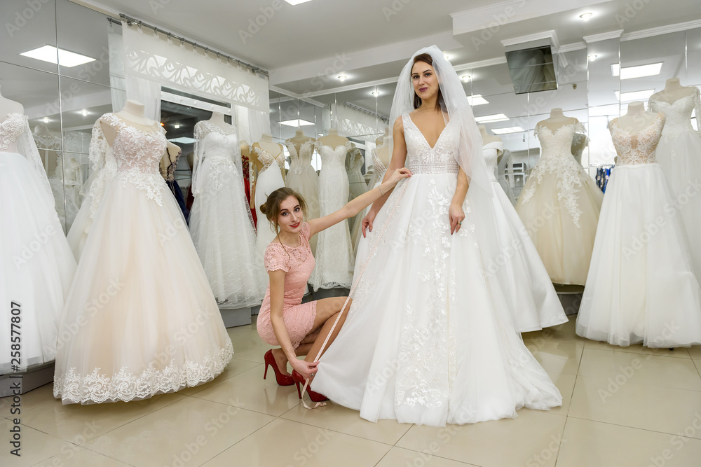 Wedding consultant helps bride fit wedding dress in salon Wedding consultant helps bride fit wedding dress in salon