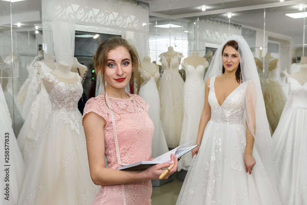 Dressmaker with notepad in wedding salon and bride