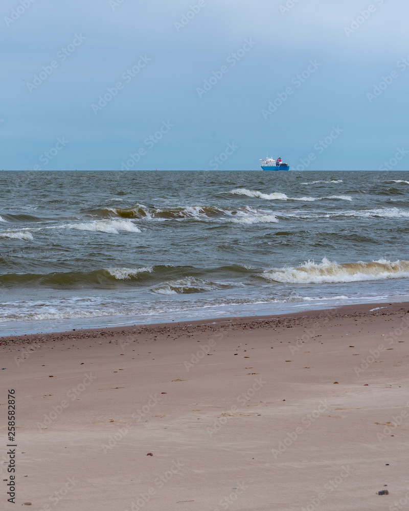 the Baltic Sea sandy beach with small stones and a large ship sailing away; beautiful blue sky above the horizon