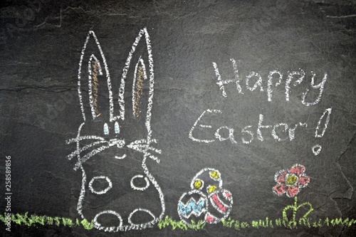 On a dark stone surface was painted a chalk and a few Easter eggs with chalk - concept with childlike drawing for Easter with Easter bunny and Easter eggs on a green meadow