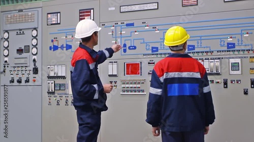 two engineers talk while showing examples on circuit at main control panel of gas compressor station, closeup