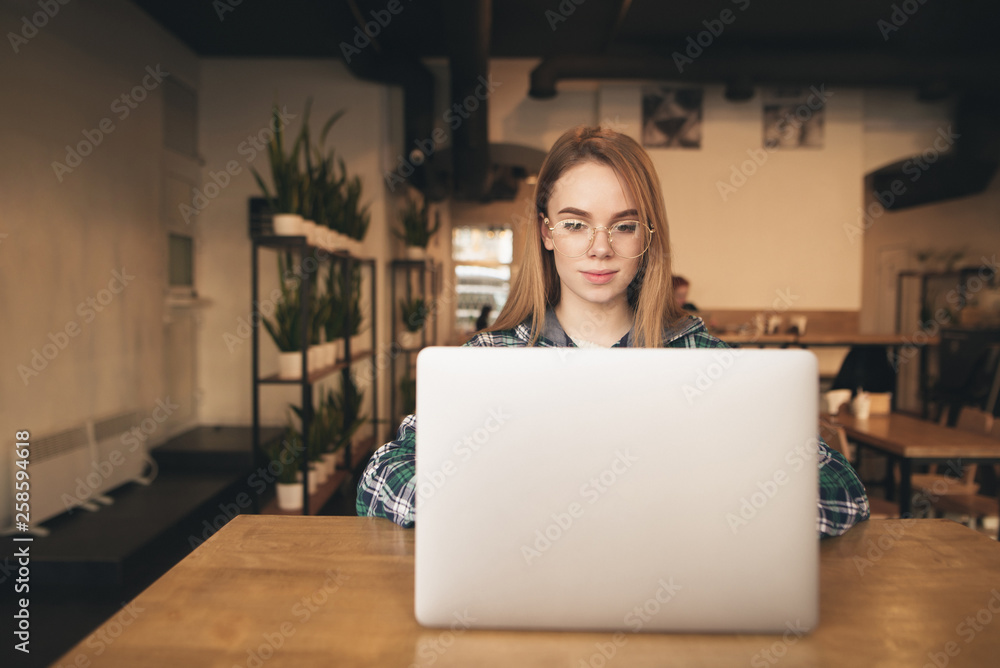 Beautiful freelance girl works in a cozy cafe on a laptop. Student girl in a shirt studying in a cafe, using the Internet on a laptop. Work in the Internet. Beautiful freelance girl works in a cozy cafe on a laptop. Student girl in a shirt studying in a cafe, using the Internet on a laptop. Work in the Internet.