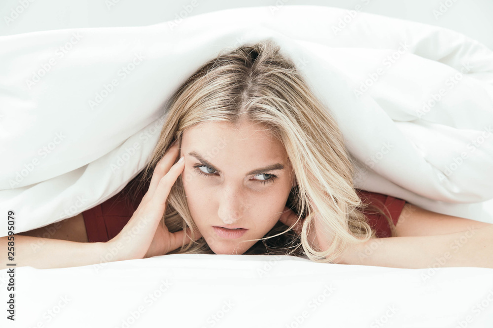 Fototapeta premium Grumpy blonde girl under white covers