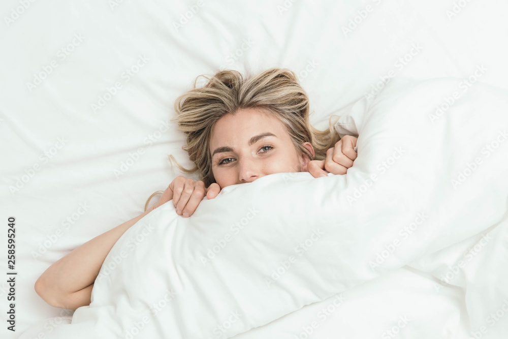 Happy Caucasian Blonde Girl Peeking from Under White Duvet Covers Happy Caucasian Blonde Girl Peeking from Under White Duvet Covers