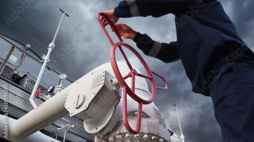 worker opens ball valve on cooling installations at gas compressor station, against background of thunderstorm sky, closeup