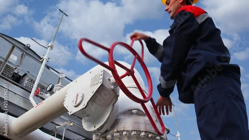 worker closes ball valve on cooling installations at gas compressor station, against background of cloudy sky, closeup