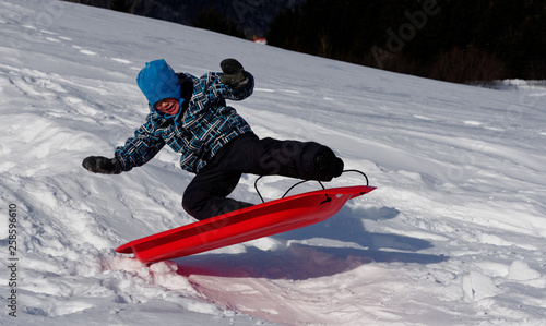Fotografie A young Boy (4 yrs old) jumping into the air on a sledge in Quebec winter