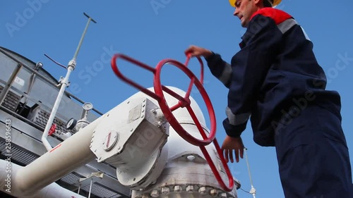 worker closes ball valve on cooling installations at gas compressor station, against background of blue sky, closeup
