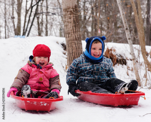 Brother and sisters (5 and 3 yrs old) sledging together in Quebec in winter photo