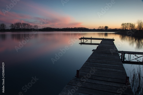Wooden jetty on a calm lake and pink clouds after sunset