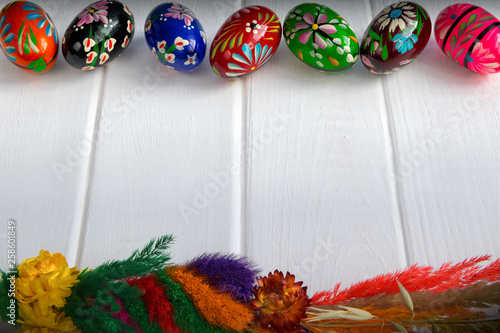 Easter frame made of colorful, wooden eggs and easter palm on white planks.