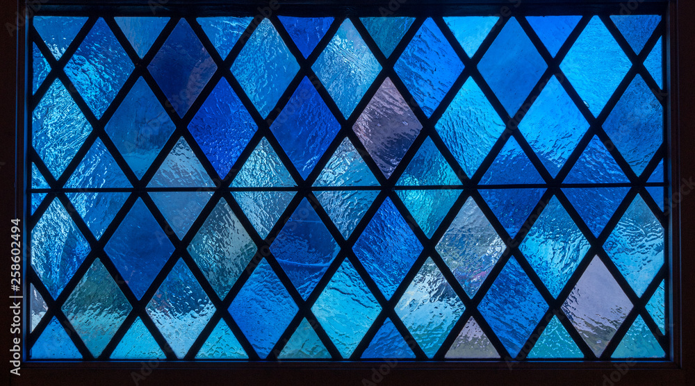 Detail of blue diamond shaped panes in colored light from stained glass window in catholic church - obrazy, fototapety, plakaty 