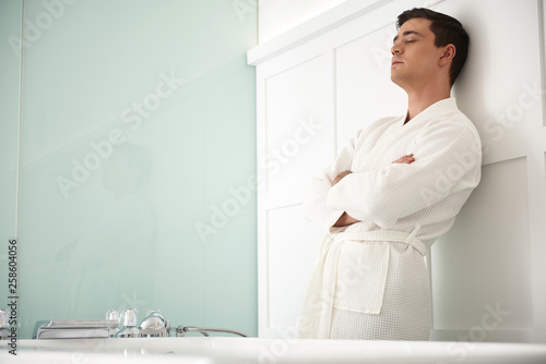 Young relaxed man leaning on wall in spa room