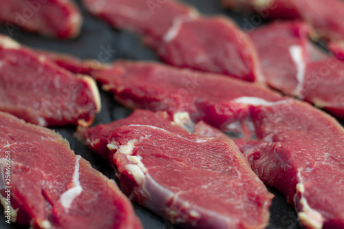 Red pieces of fresh veal, sliced into raw thin beef steaks, laid out on a wooden board. Raw beef for steaks with streaks of fat.