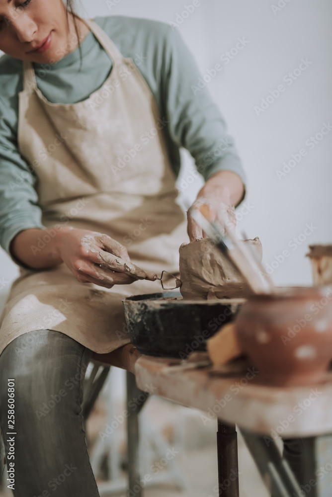 Young lady using sculpture scraper knife while making clay pot
