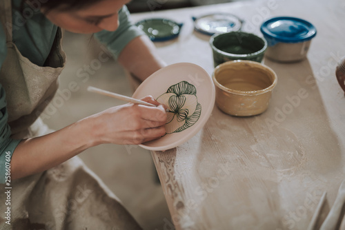 Billede på lærred Young lady in apron painting ceramic plate at workshop