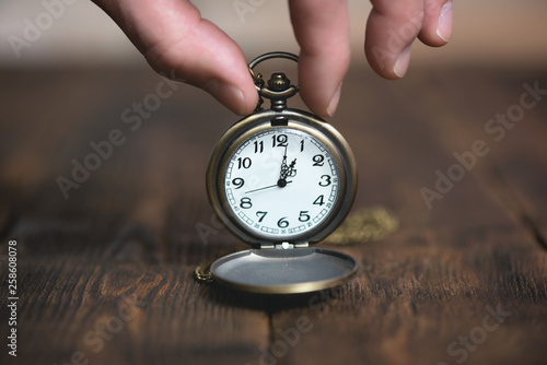 Man is holding in hand a pocket watch on a brown table background.