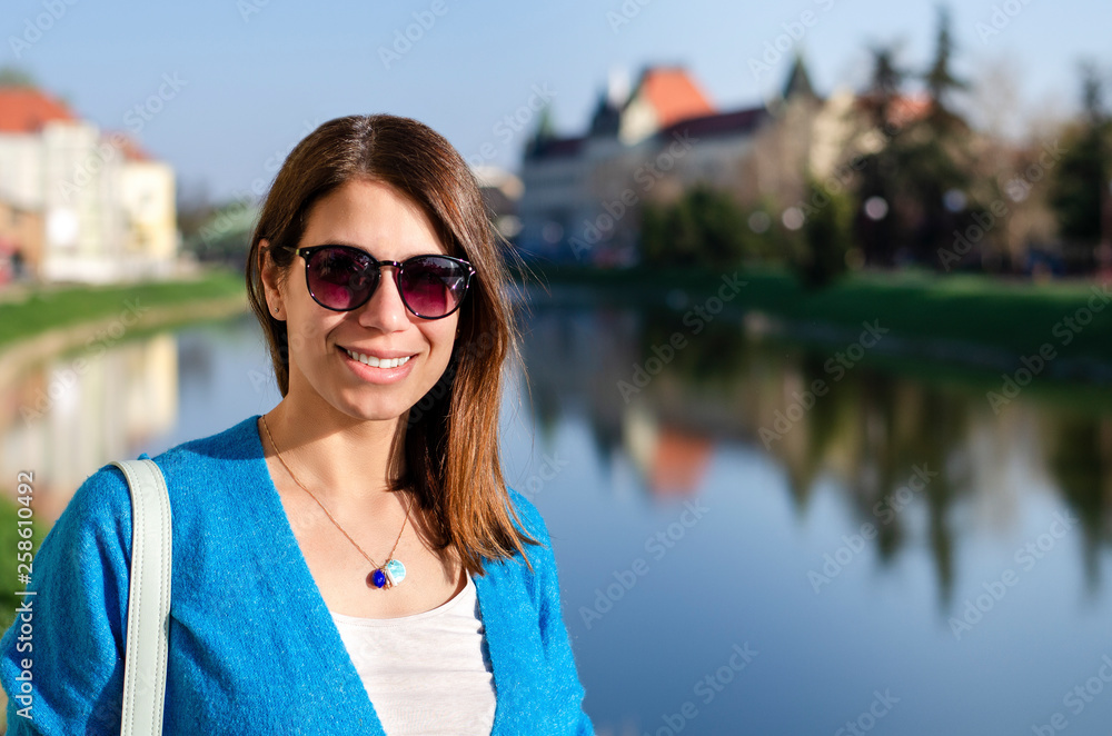 Portrait of a gorgeous young woman traveler wearing sunglasses on a bright sunny day in a city in Europe
