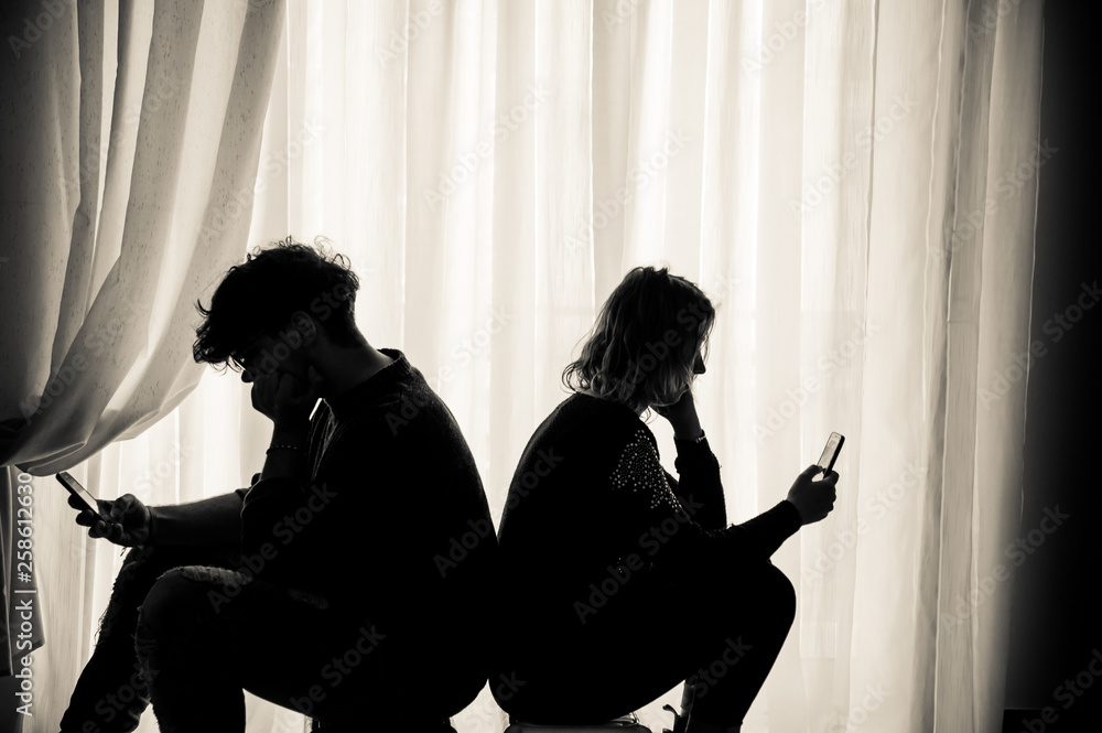 Teenagers sitting back to back looking at their cell phones, sepia effect
