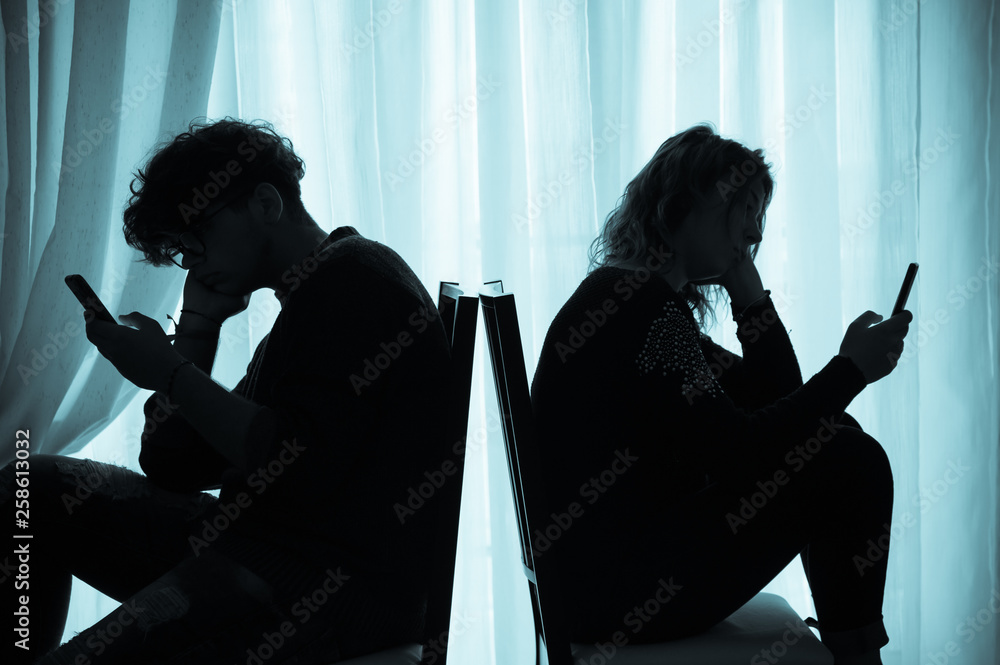 Teenagers sitting back to back looking at their cell phones, cold effect