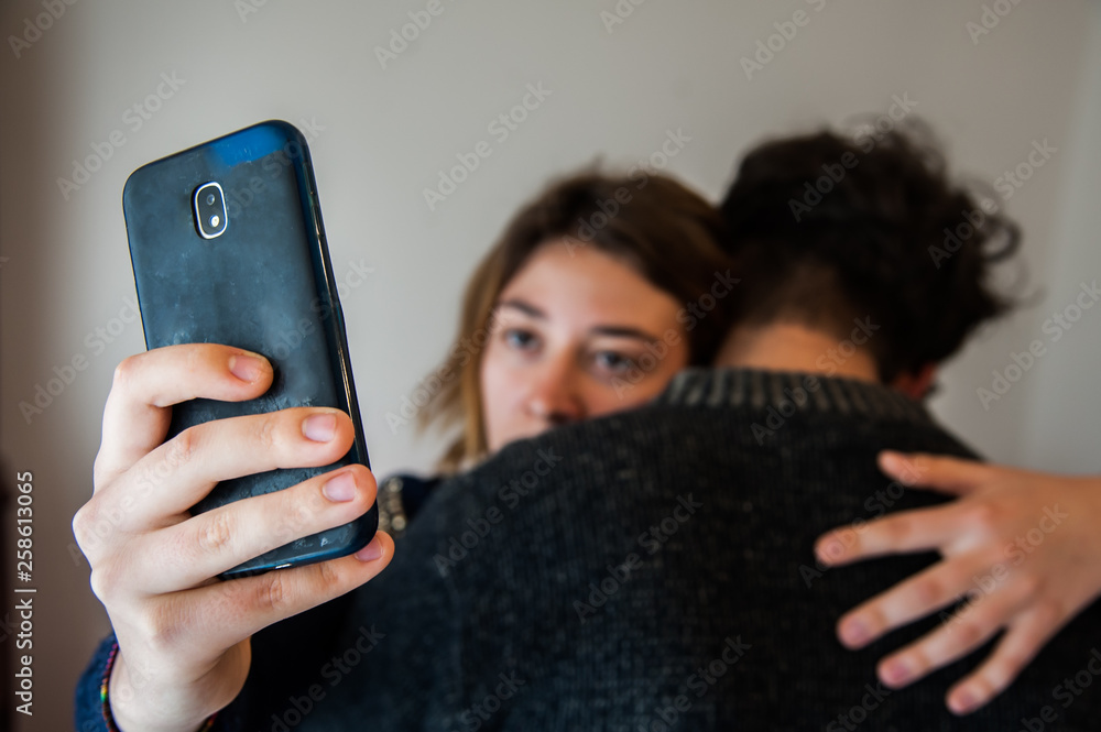 Girl looking at her cell phone while hugged to her boyfriend - obrazy, fototapety, plakaty 