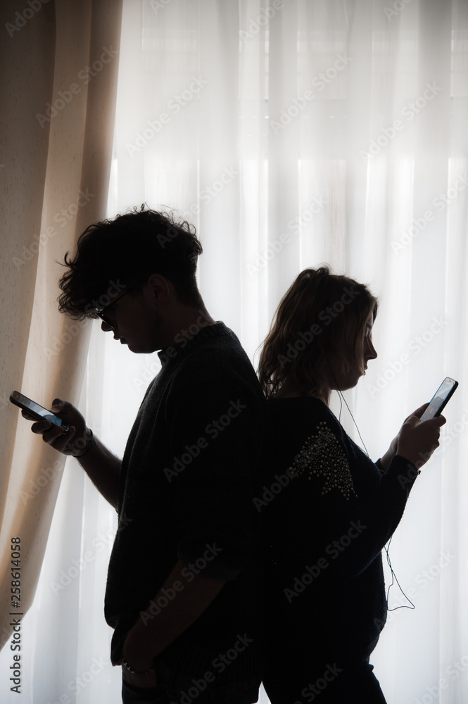 Silhouette of two teenagers with cell phones standing back to back
