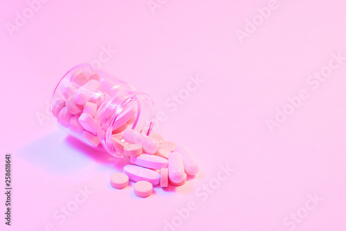 Opioid epidemic, painkillers and drug abuse concept with close up on a bottle of prescription drugs and hydrocodone pills falling out of it on glowing neon background