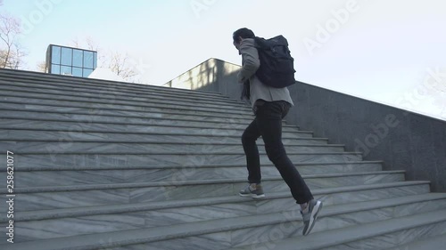 Young male businessman with backpack run on the stairs outdoors and talk with cellphone 