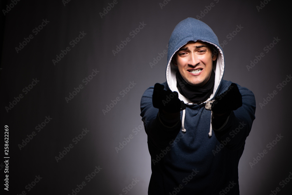 Young gangster in hood on grey background 