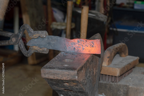 This piece of hot metal is being forged into shape to one day be a collectible and useable fixed blade knife. Bokeh background.