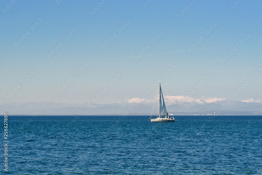 Sailing boat in the Adriatic Sea in front of Piran in Slovenia, with the Alps and the Dolomites covered with snow in the background, blue sea and blue sky, wallpaper with copy space