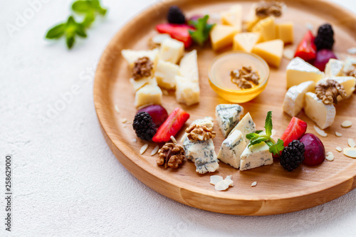 cheese plate, delicious appetizer to wine with fruits, nuts, honey, served on a light wooden board. camembert, parmesan, dorblu and maasdam  slices, gourmet food, banquet