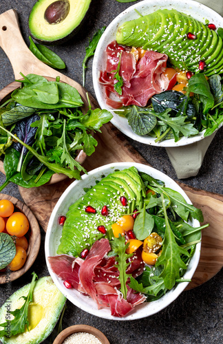 Low carbs bowl. Fresh salad with green spinach, rucola, avocado an ham serrano in white bowl, gray background, top view photo