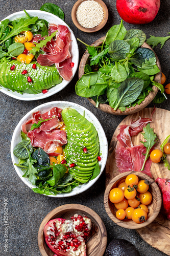 Low carbs bowl. Fresh salad with green spinach, rucola, avocado an ham serrano in white bowl, gray background, top view