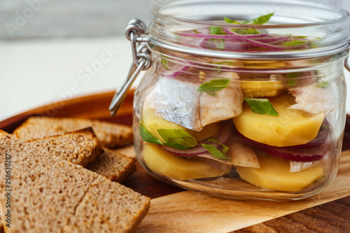 herring and potato appetizer with red onion in glass jar served with rye bread toasts. fish snack, holiday salad. nourishing and tasty food. 