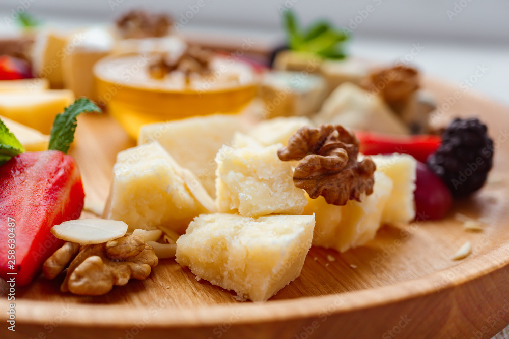 Cheese plate. slices of parmesan, dorblu, camembert and maasdam served with walnuts and honey on wooden board Cheese plate. slices of parmesan, dorblu, camembert and maasdam served with walnuts and honey on wooden board