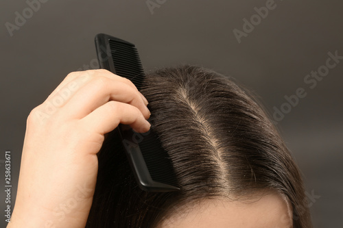 Woman with comb and dandruff in her dark hair on grey background, closeup