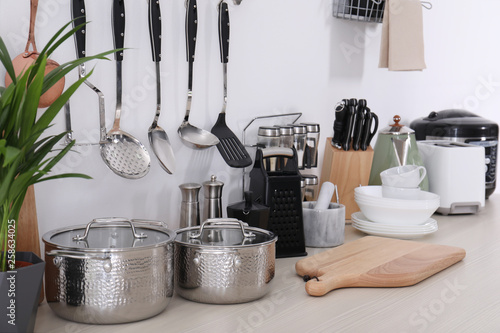 Set of clean cookware, dishes, utensils and appliances on table at white wall photo