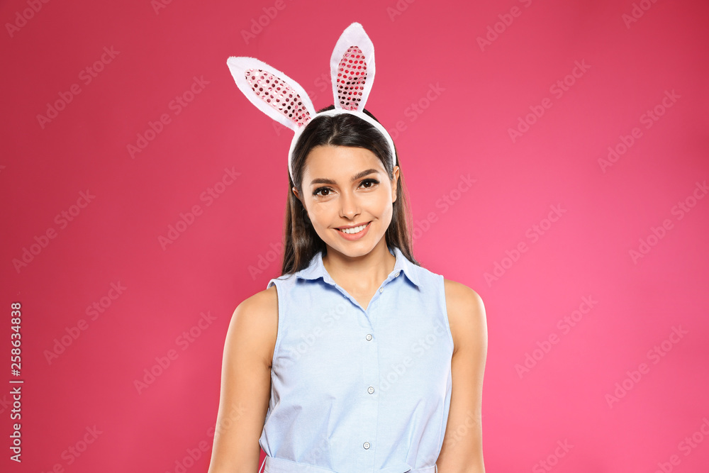 Portrait of beautiful woman in Easter bunny ears headband on color background