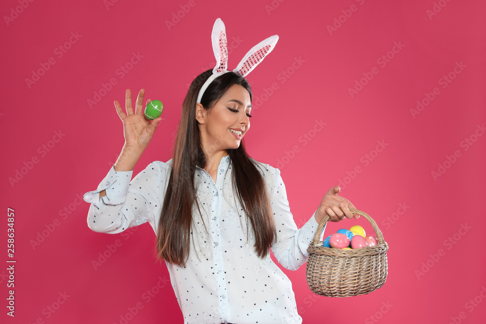 Beautiful woman in bunny ears headband with basket of Easter eggs on color background Beautiful woman in bunny ears headband with basket of Easter eggs on color background
