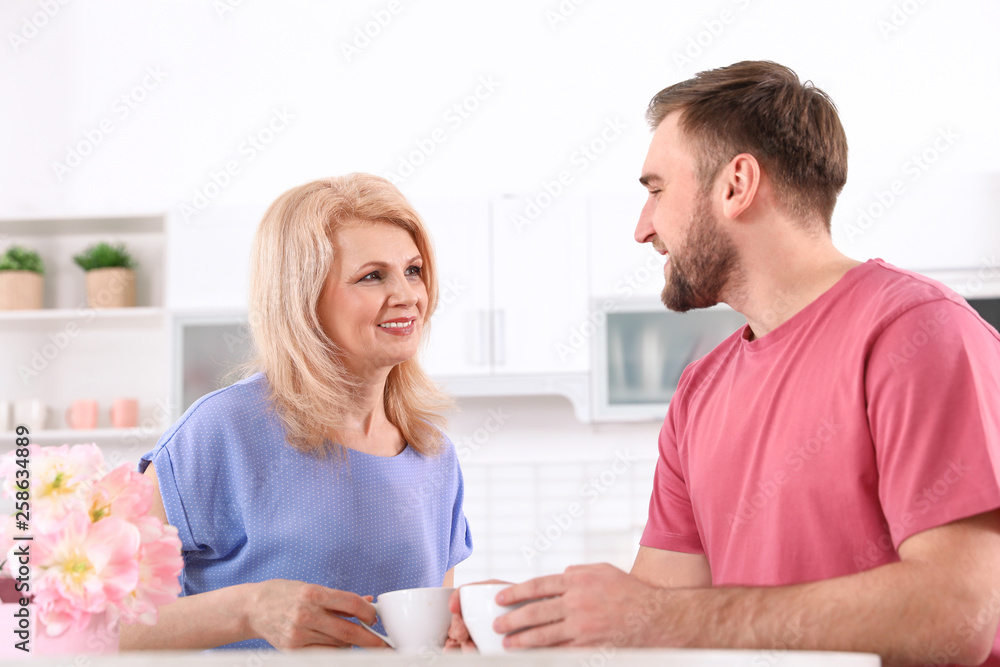 Young man and his mature mom having breakfast in kitchen. Happy Mother's Day Young man and his mature mom having breakfast in kitchen. Happy Mother's Day