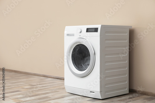 Modern washing machine with laundry near color wall, space for text