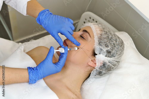Aesthetic cosmetology. Hands of cosmetologist inject hyaluronic acid into cheekbone area of girl.