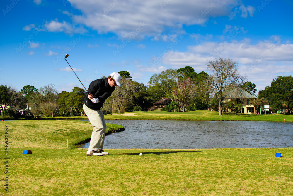 Obraz premium Golfer in action shot hitting with ball on tee in front of water