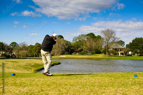 Slika na platnu Golfer in action shot hitting with ball heading towards the pin hole over water