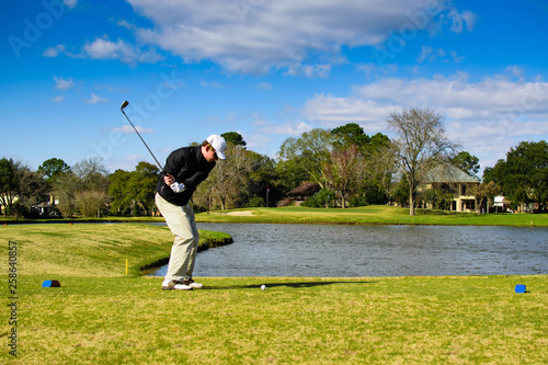 Golfer in action shot hitting with ball on tee in front of water